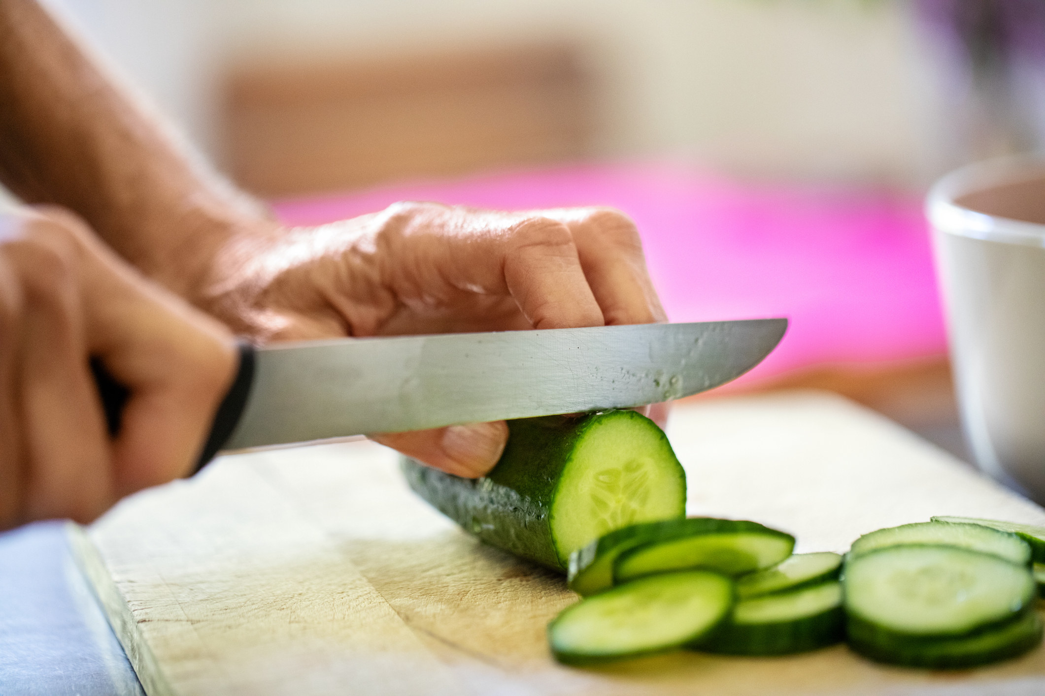 A person slicing a cucumber with a knife.