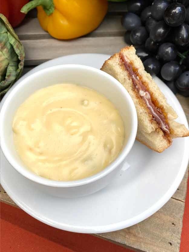 close-up of soup in bowl on a plate with the sandwich next to it