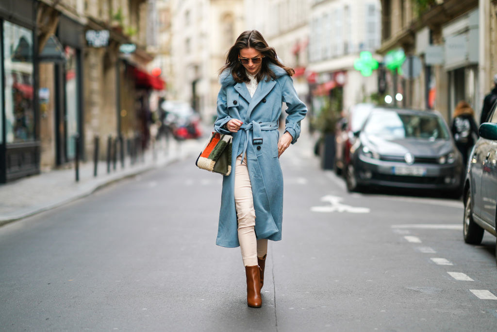 Woman in a blue trench coat and brown boots walking down street in Paris
