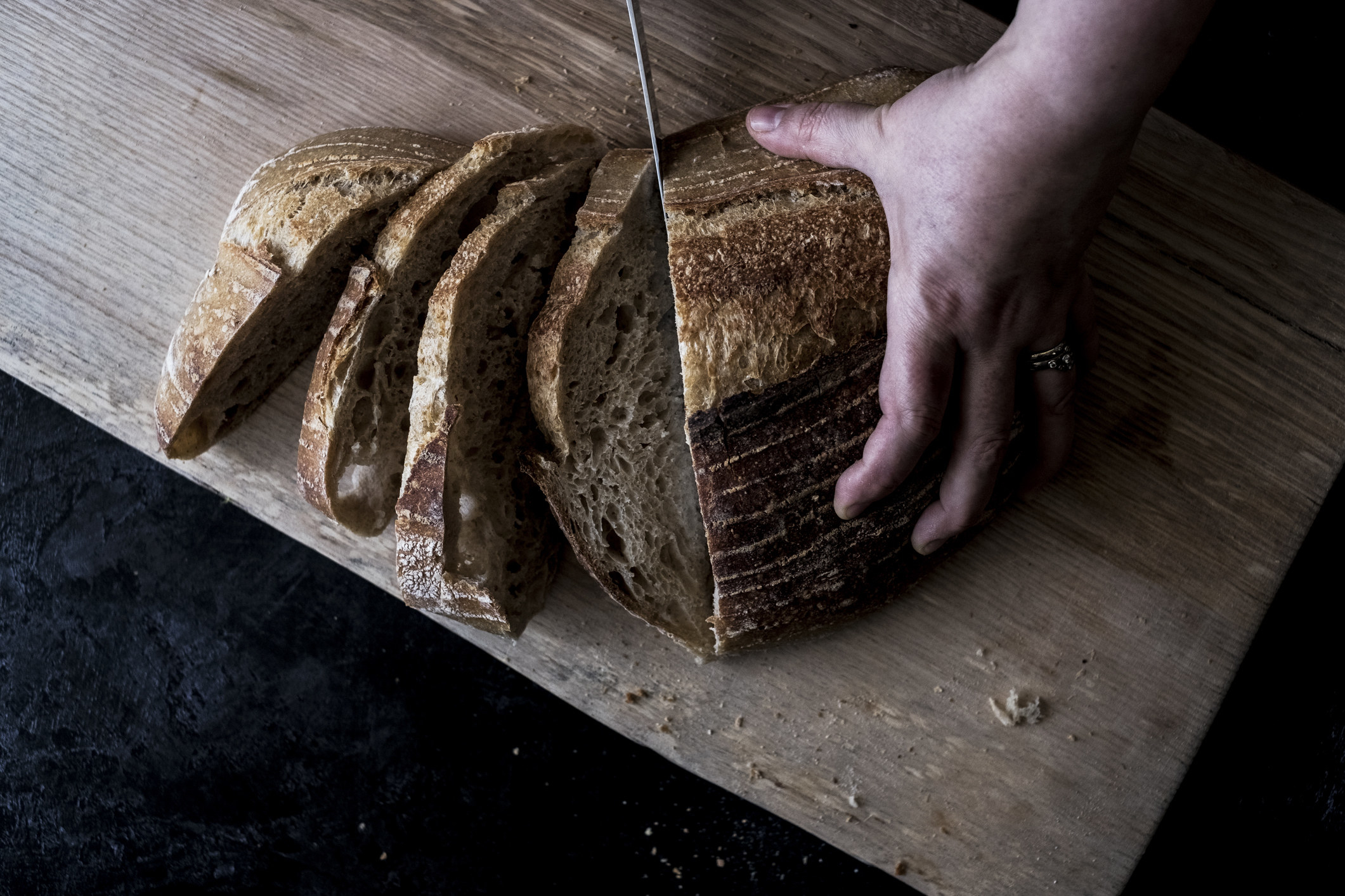 A hand holding a loaf of bread and using a breadknife to cut slices.