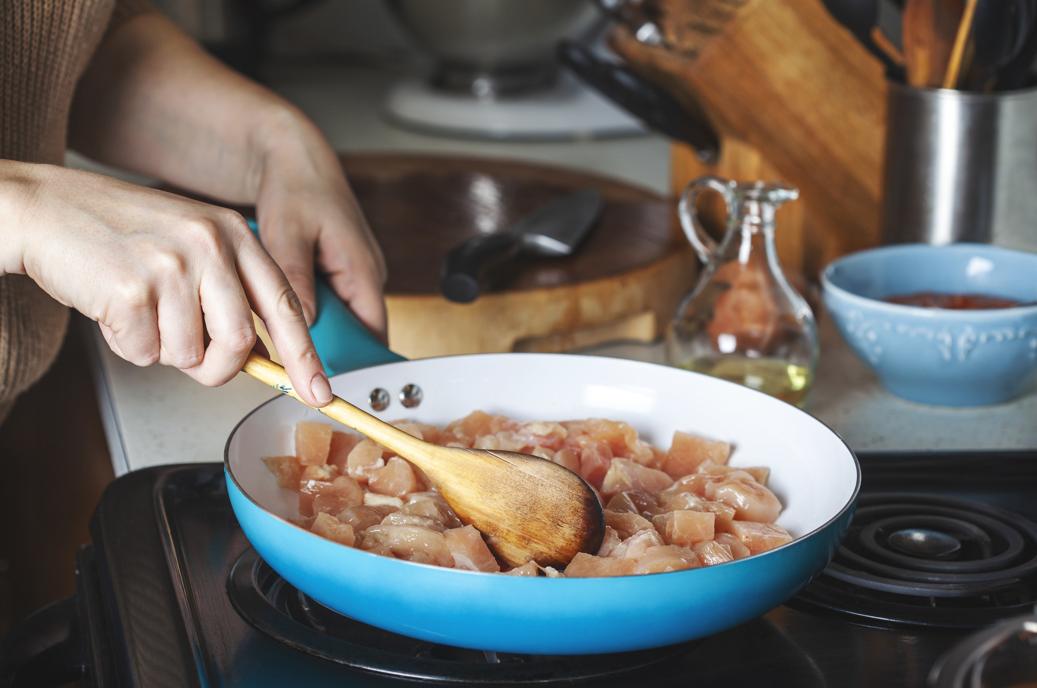 A woman frying chicken breast in a skillet.