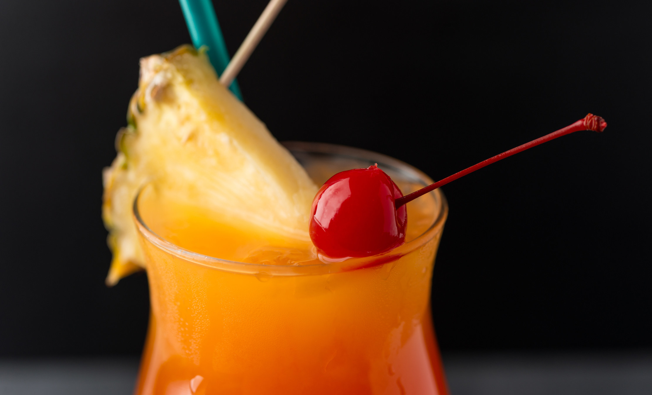 A colorful drink with a pineapple and a cherry on top