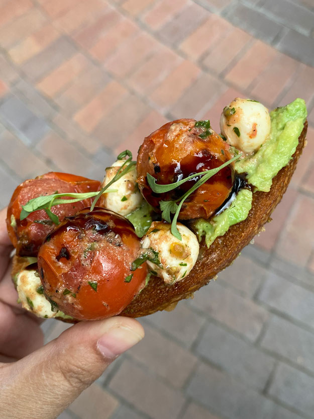 close-up of a toasted slice of bread with avocado, cherry tomatoes, and mozzarella balls