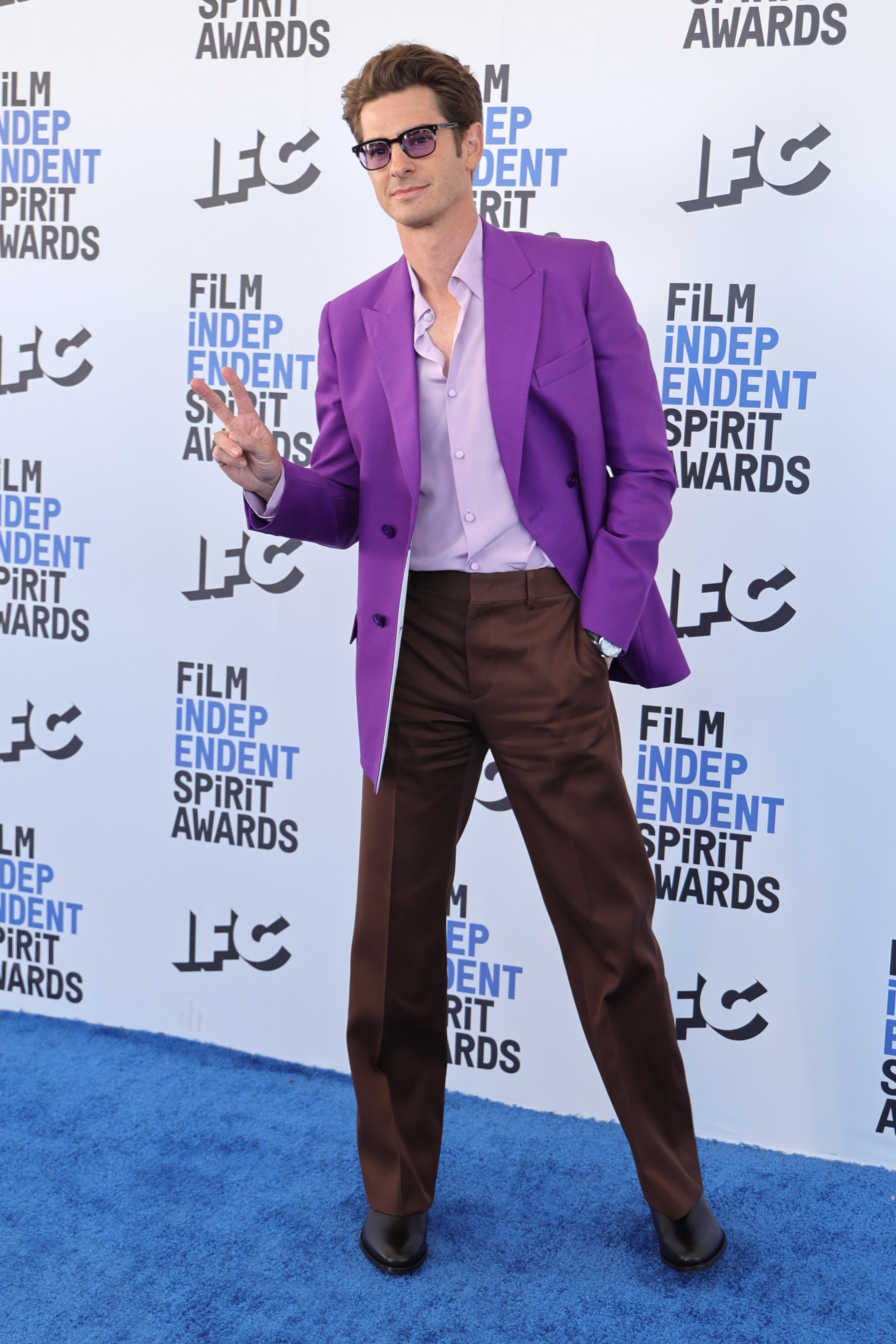Andrew wears a purple suit jacket and brown pants