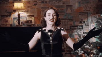Mrs Maisel raising her arms and smiling