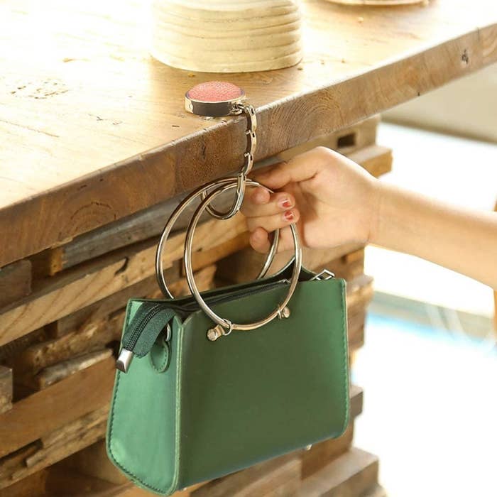 A person hanging their purse on a bag hook on a table