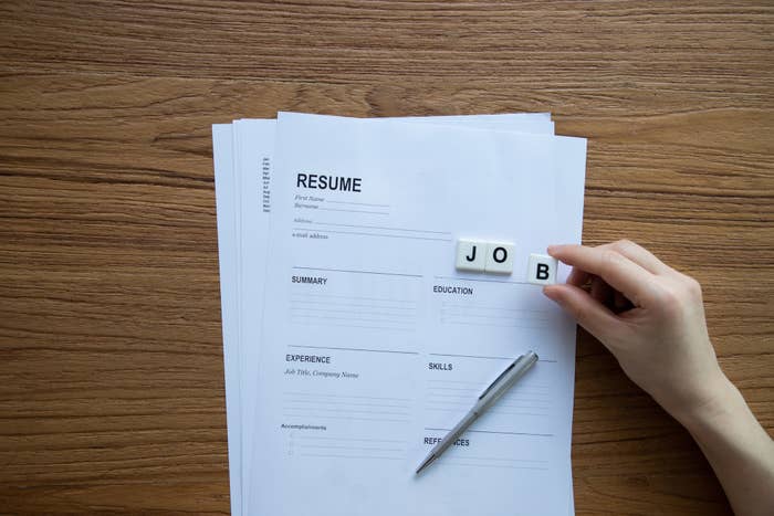 A printed resume on a table with someone holding wooden blocks that spell out &quot;job&quot;
