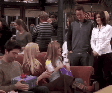 Gif from Friends of Joey, Phoebe, and Rachel opening gifts while Monica and Chandler watch and smile