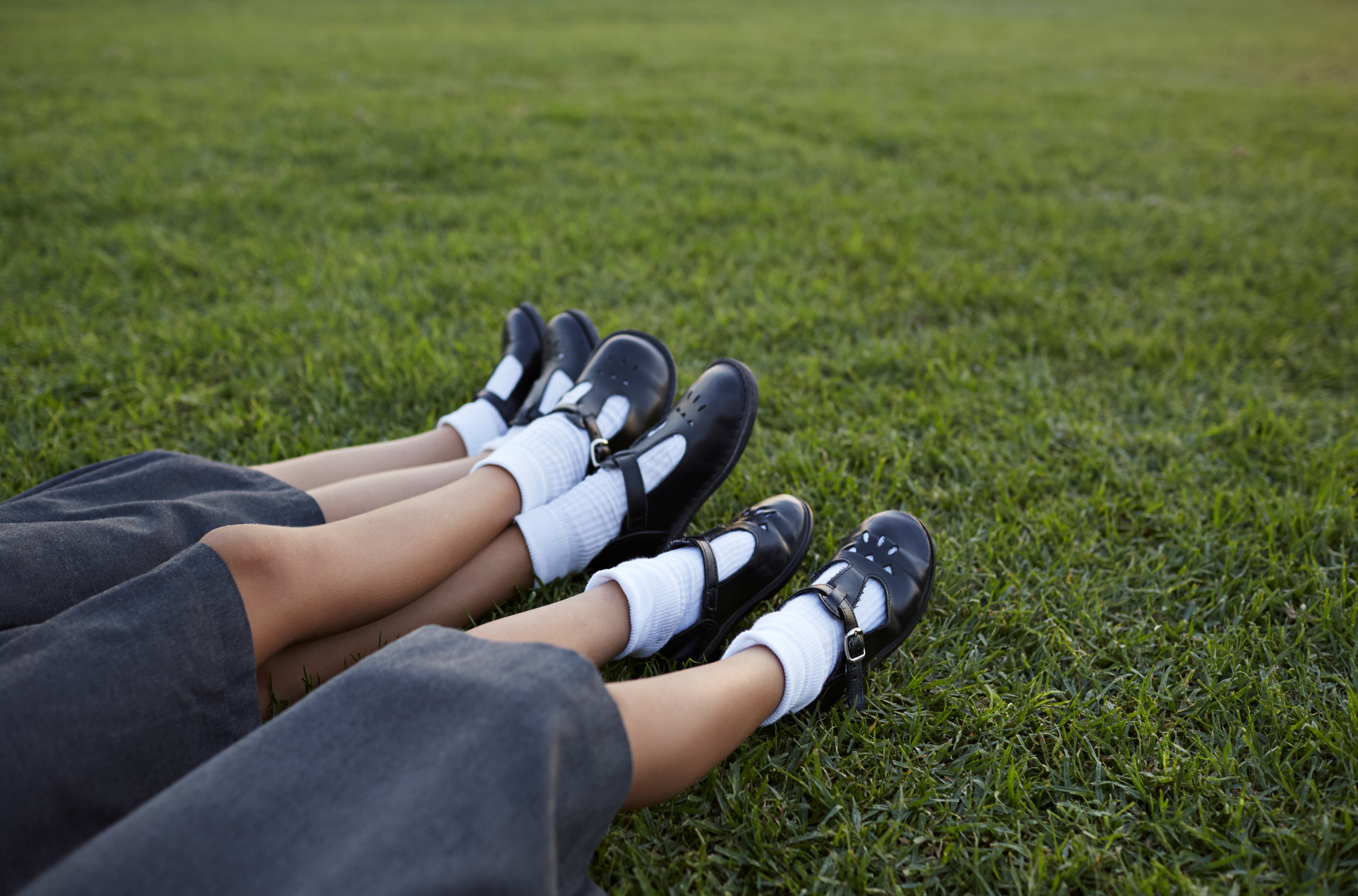 Three pairs of children&#x27;s legs in school uniforms lying on the lawn