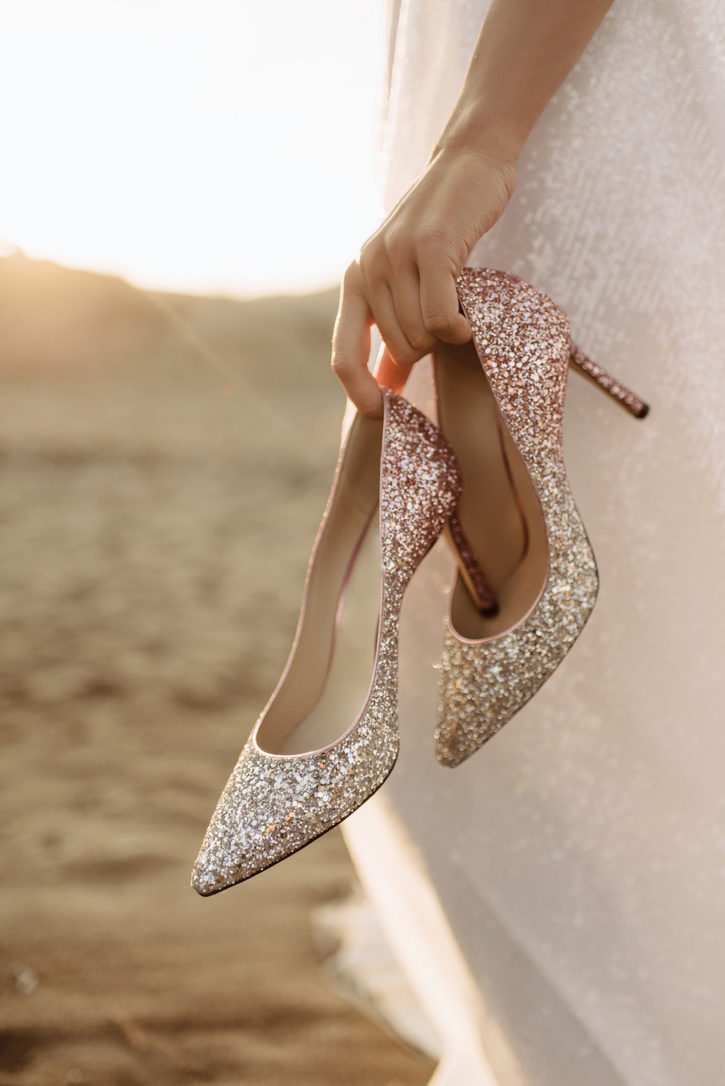 Close-up photo of bride holding high heel shoes as she walks