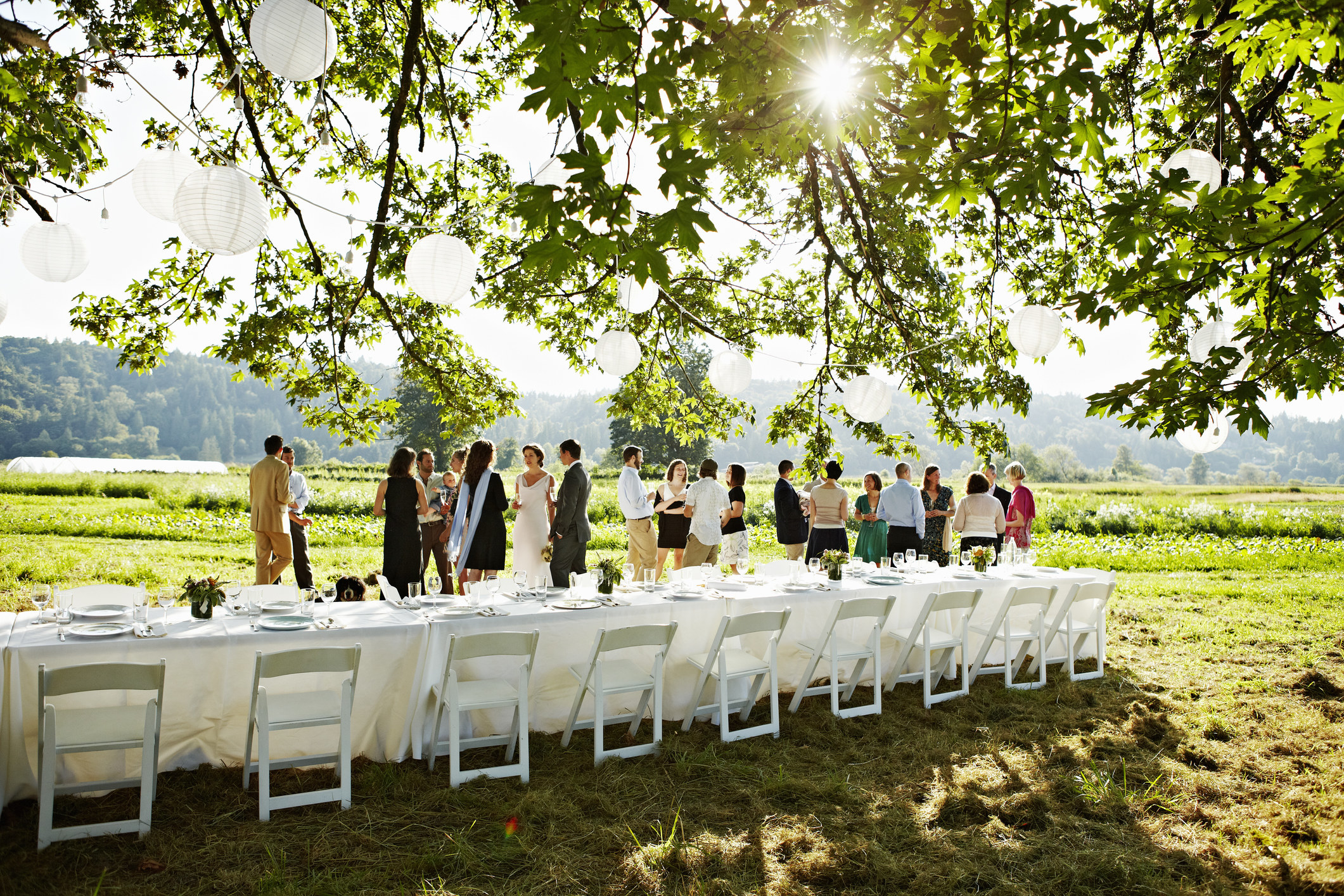 a group gathering outside along a long table set for a dinner