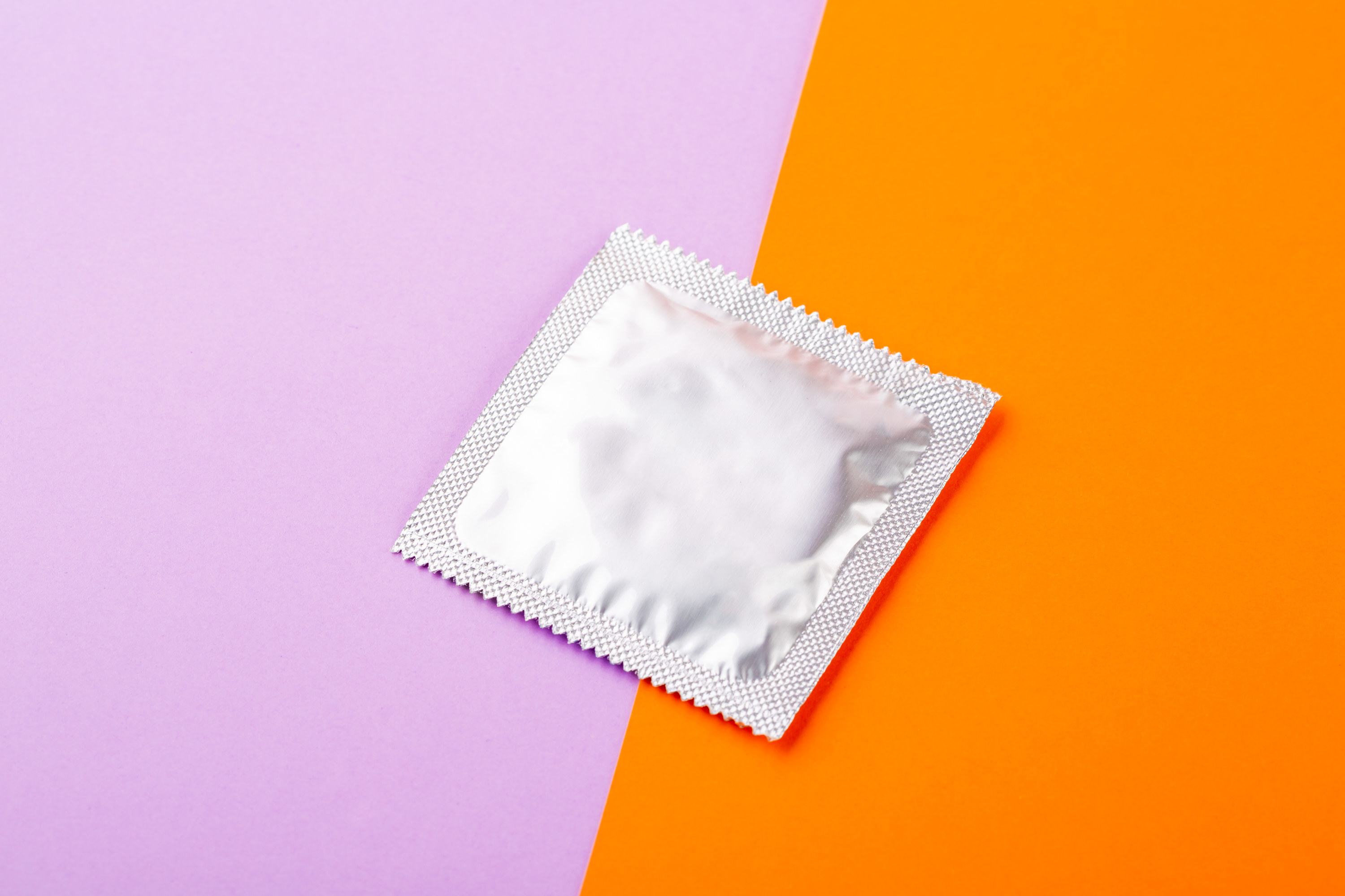 A condom wrapper against an orange and purple background