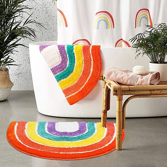 A rainbow rug outside of a bathtub in a bathroom with one draped over the tub