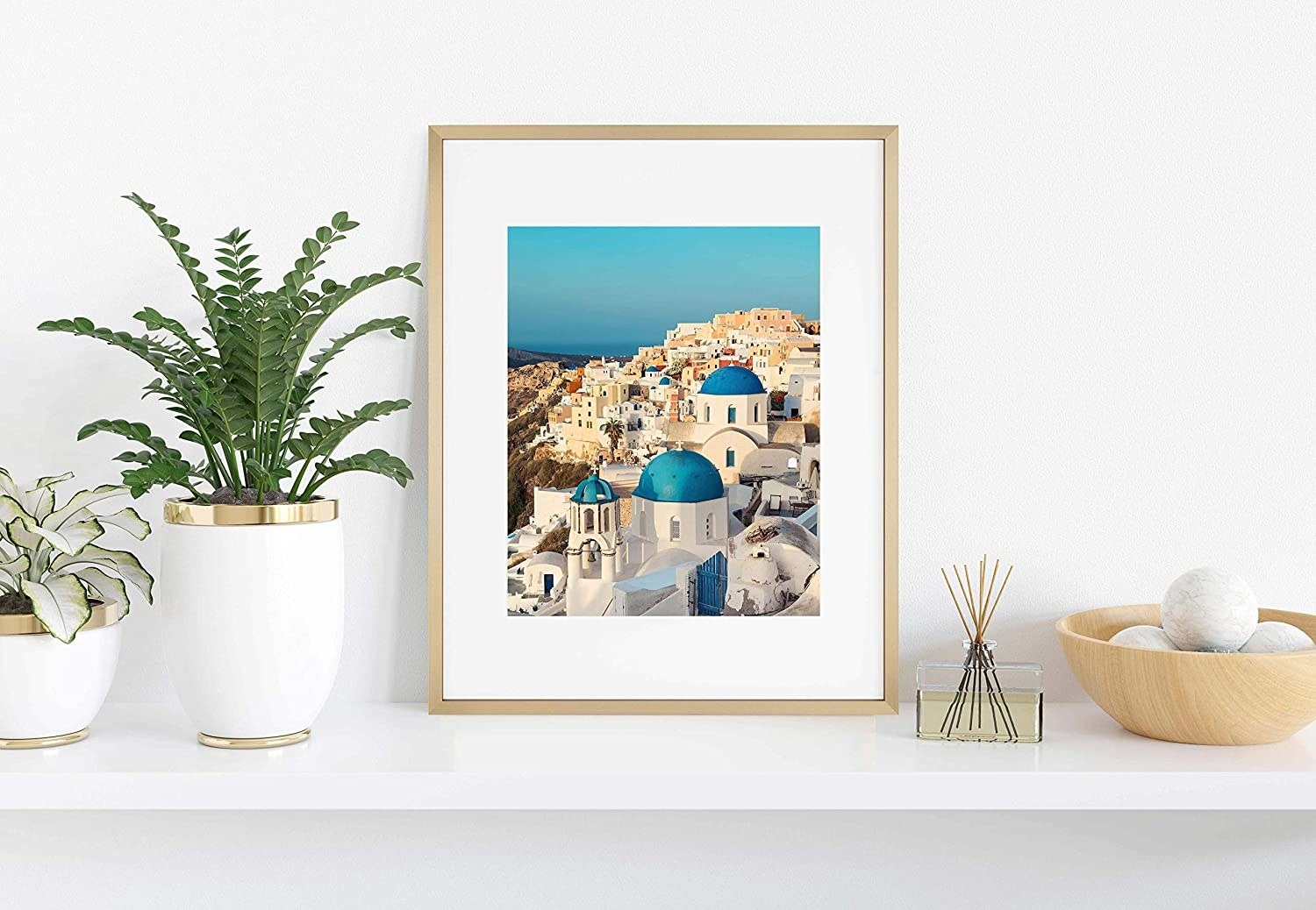 A frame with a photo in it leaning against a wall while it sits on a table with plants and trinkets