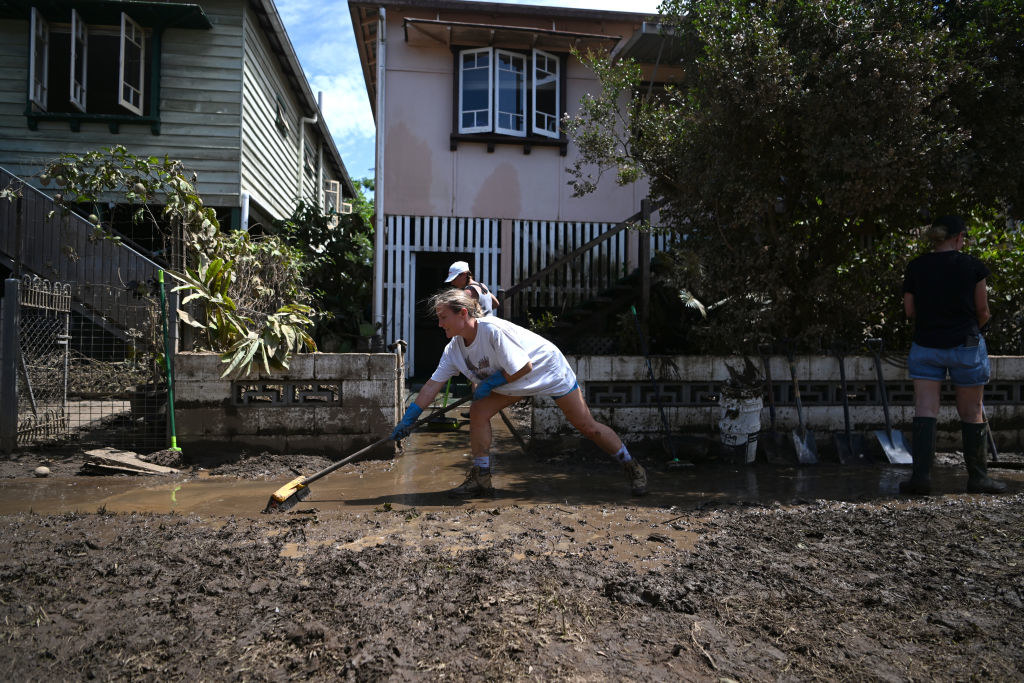 Volunteers sweep mud from the front of a flood-affected house