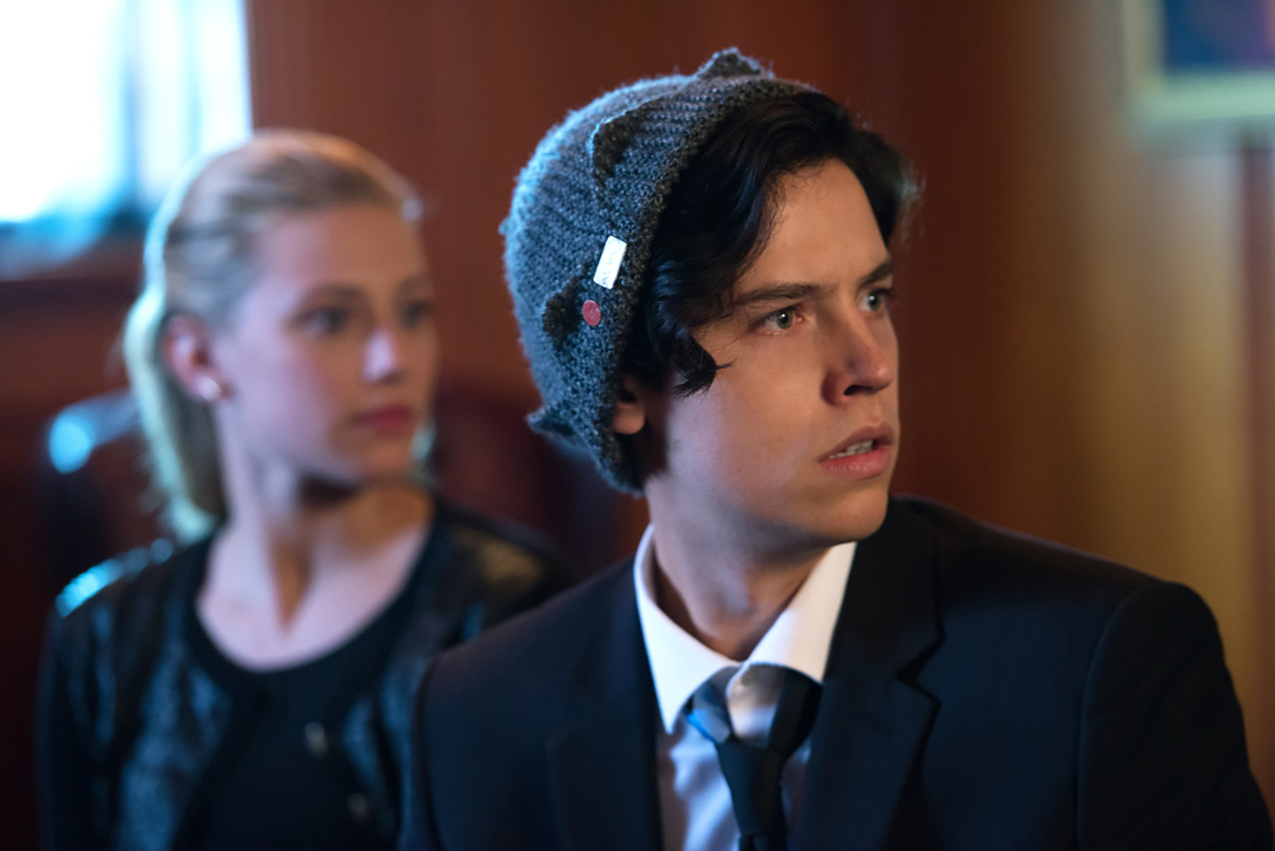 Jughead looks to his left wearing a beanie and a suit