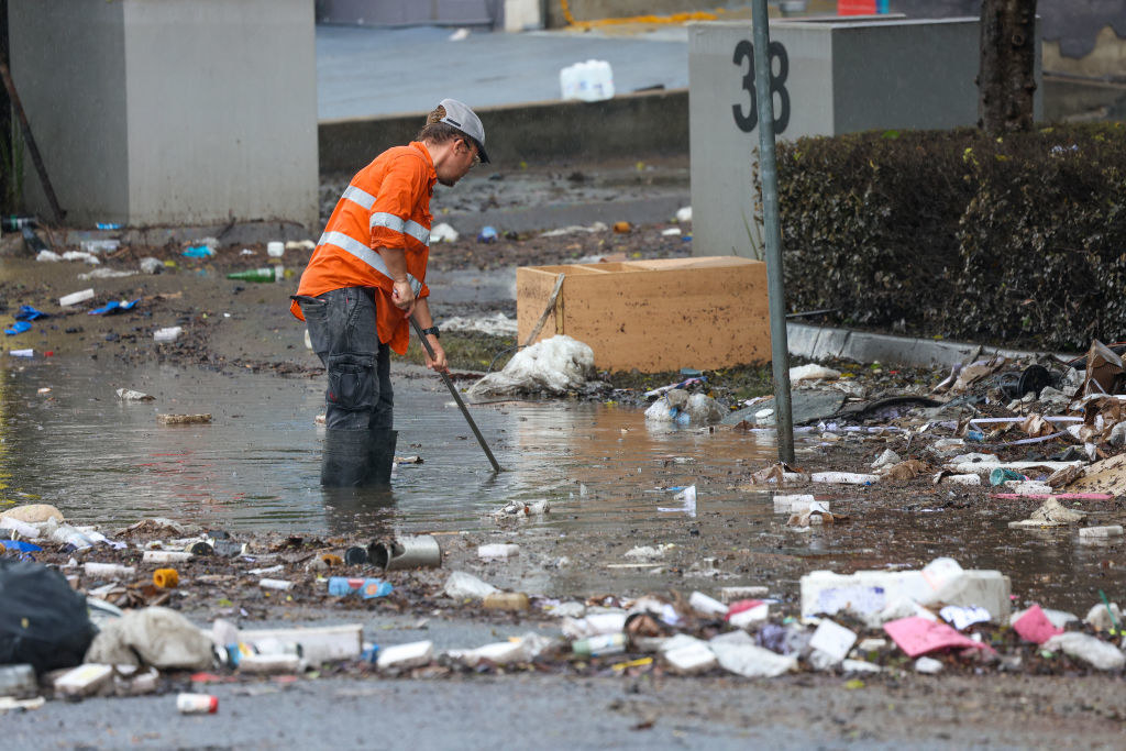 A man tries to clear drains in Brisbane; he is surrounded by rubbish