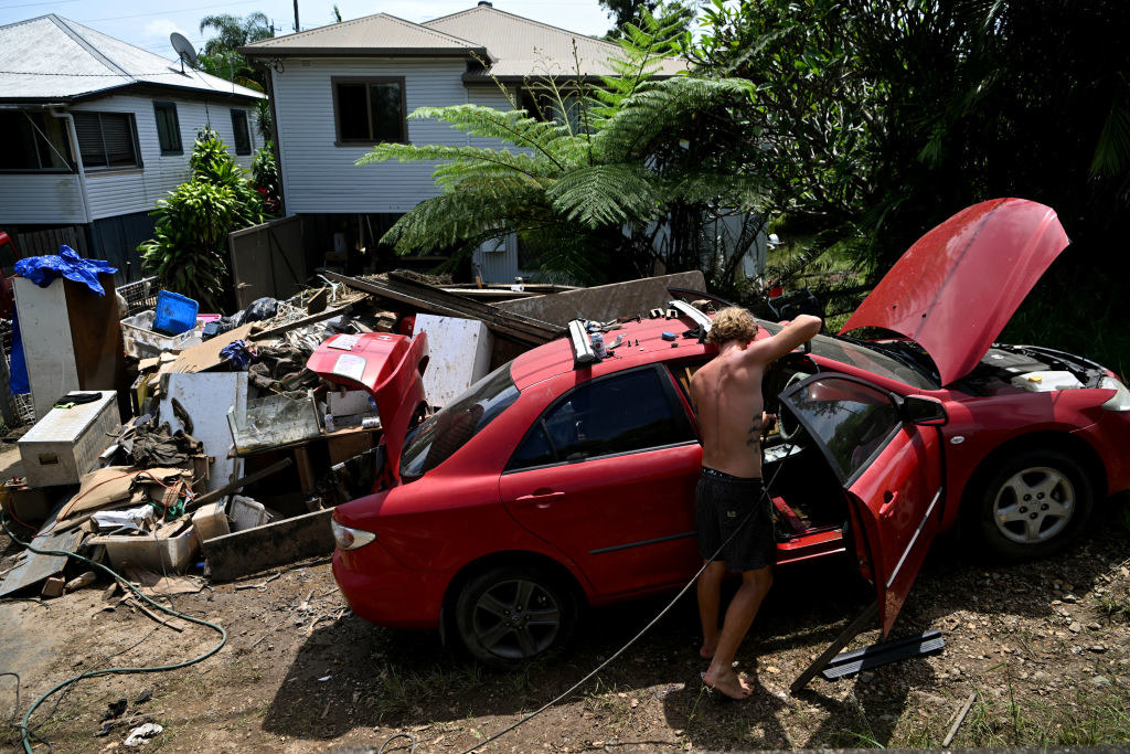 A man pressure hoses the inside of his flood-damaged car outside his home