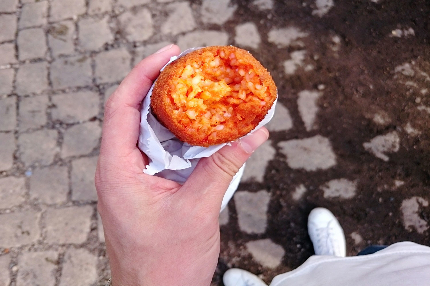 A hand holding a suppli filled with tomato risotto