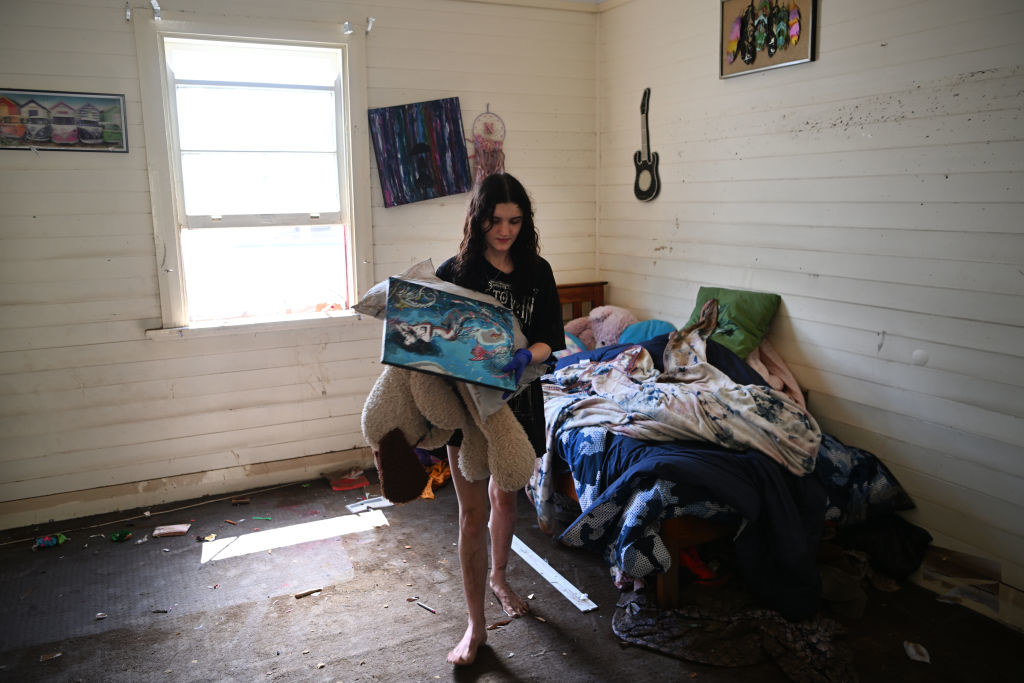 A woman removes damaged items from her sister&#x27;s bedroom in their flood-affected house