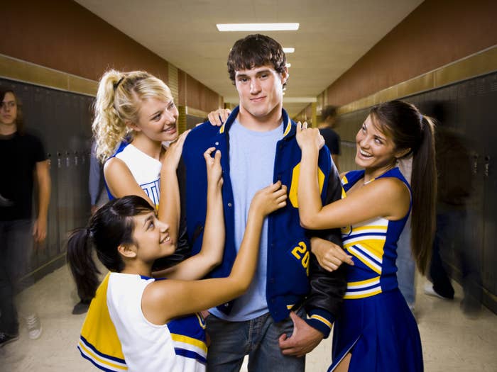 A football jock is fawned over by cheerleaders