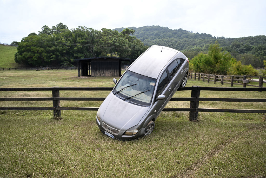 A car rests on a fence after it was carried there by floodwater
