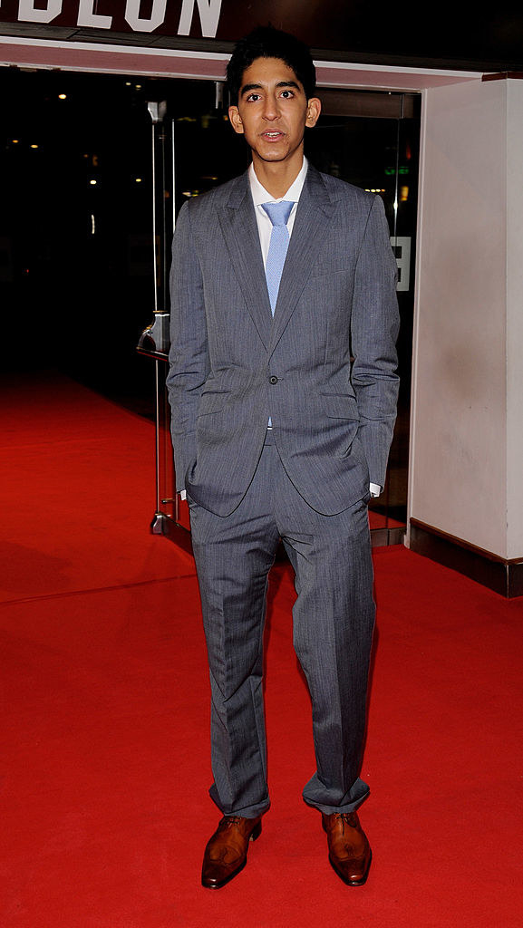 with his hands in his pockets, Dev wears his uniform blazer and matching, ill-fitting suit trousers on the red carpet