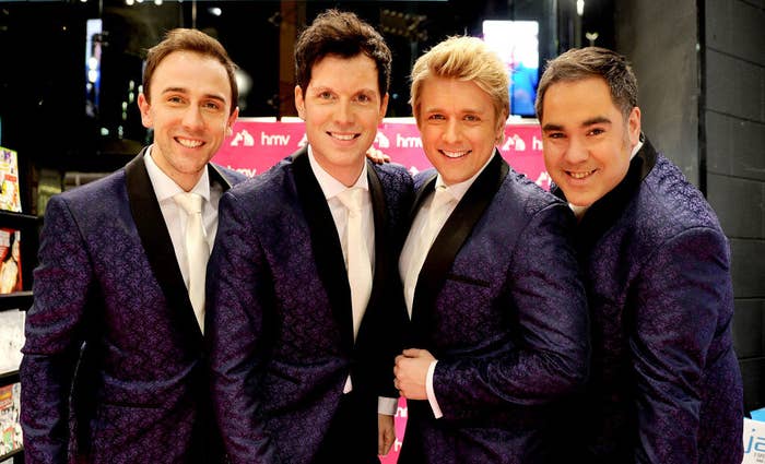 4 men standing side-by-side making up the band G4. They are all wearing purple matching suits, and white shirts and are smiling at the camera