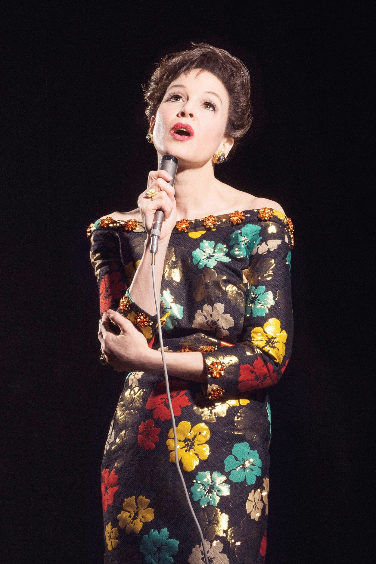 renee in a floral dress with short hair singing