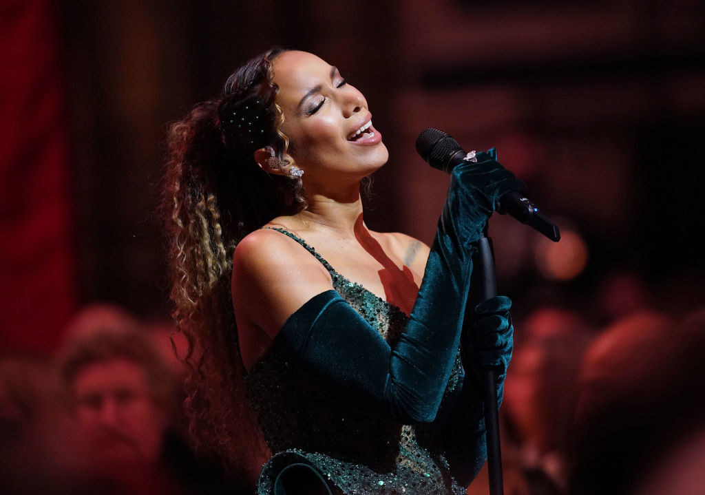 Leona Lewis performing on stage in an emerald green dress with match arm length gloves. Her hair is tied back and she&#x27;s holding the mic with both hands
