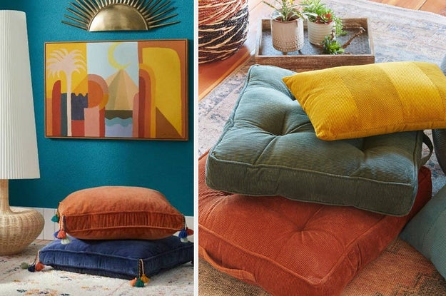 Orange and blue tasseled floor pillows stacked next to a tall lamp, three different colored floor pillows stacked on the floor