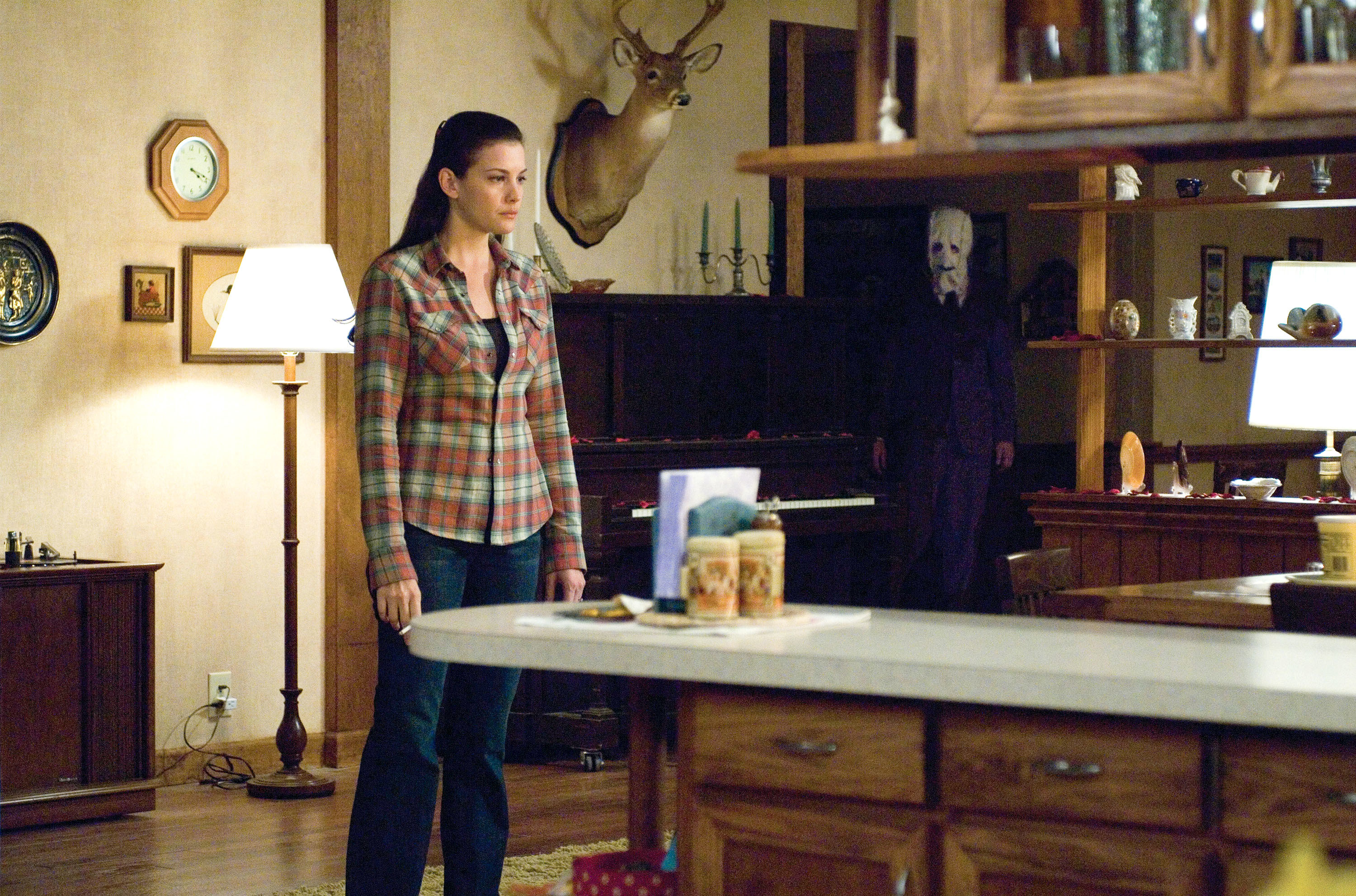 丽芙·泰勒站在一个房间和一个男人在一个可怕的面具,在她身后,面对她
