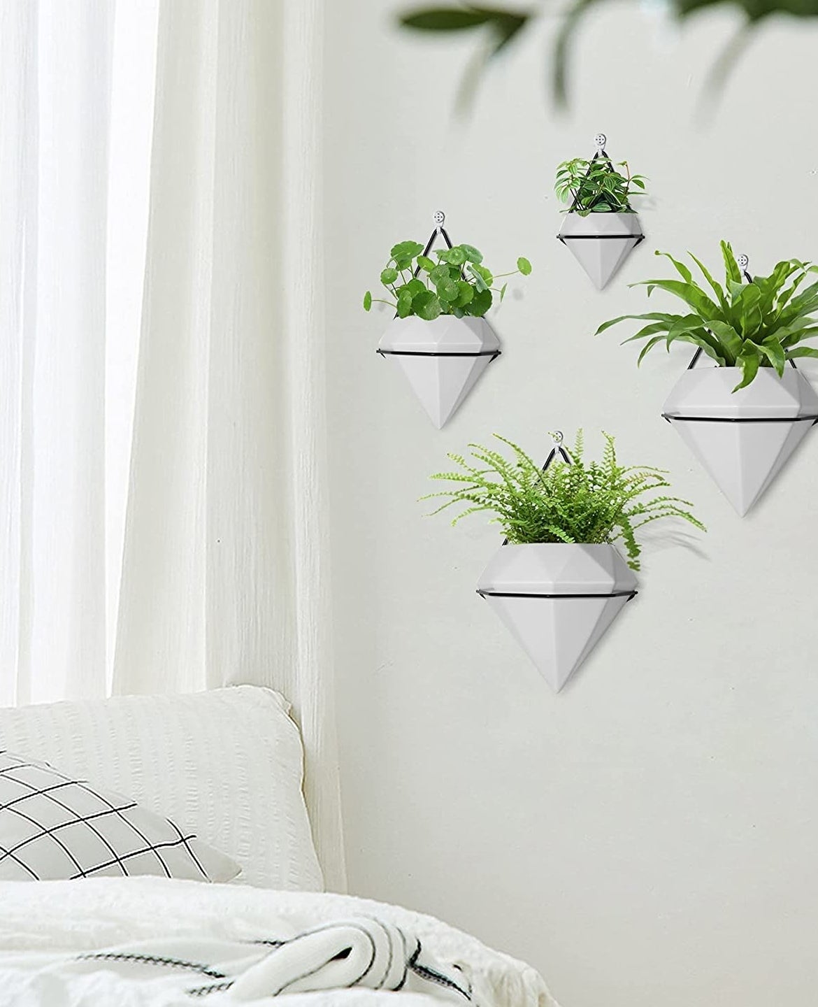 A set of four planters hanging on a bedroom wall with plants in them.