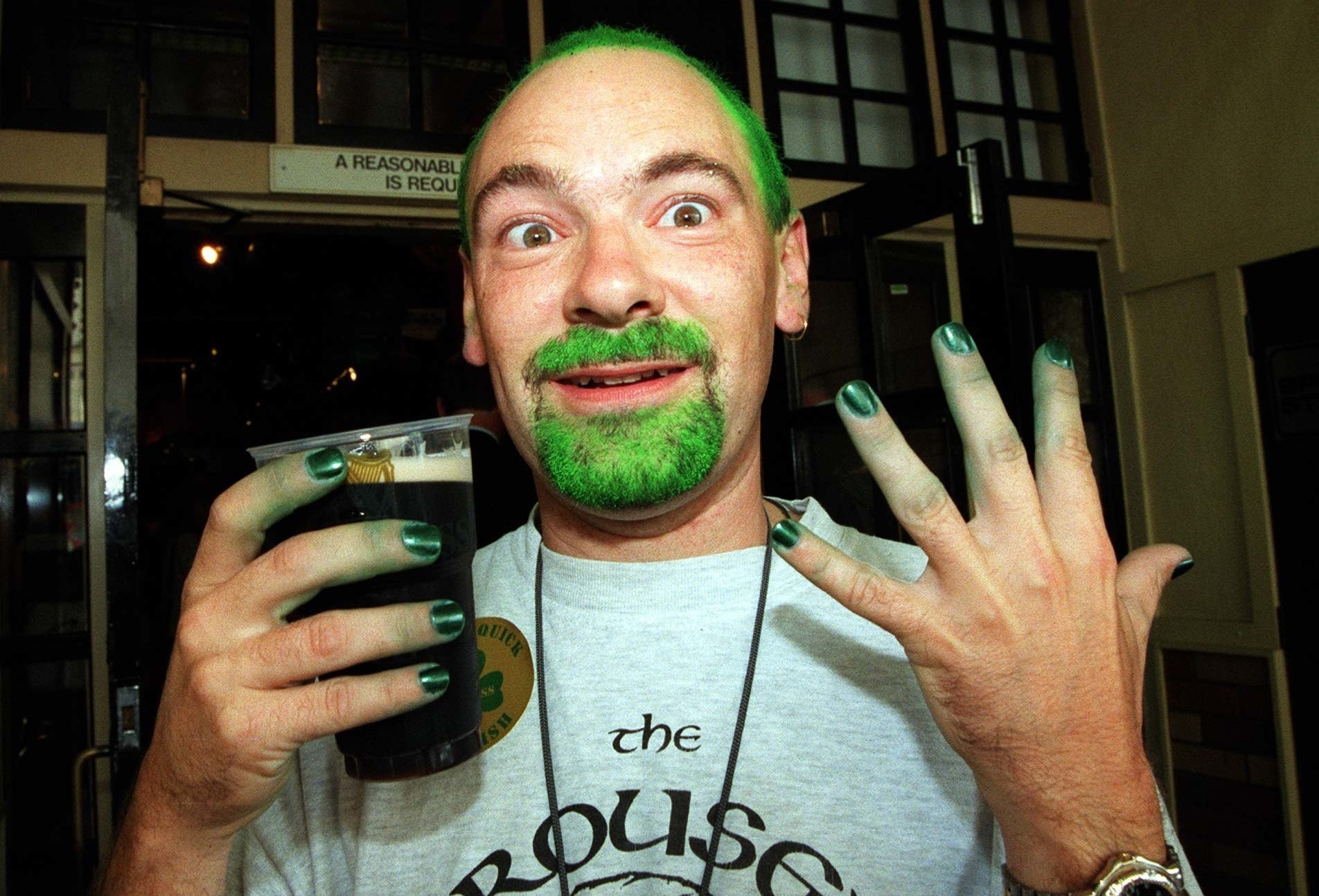 a man with green fingernails and green hair holds up a beer for the camera