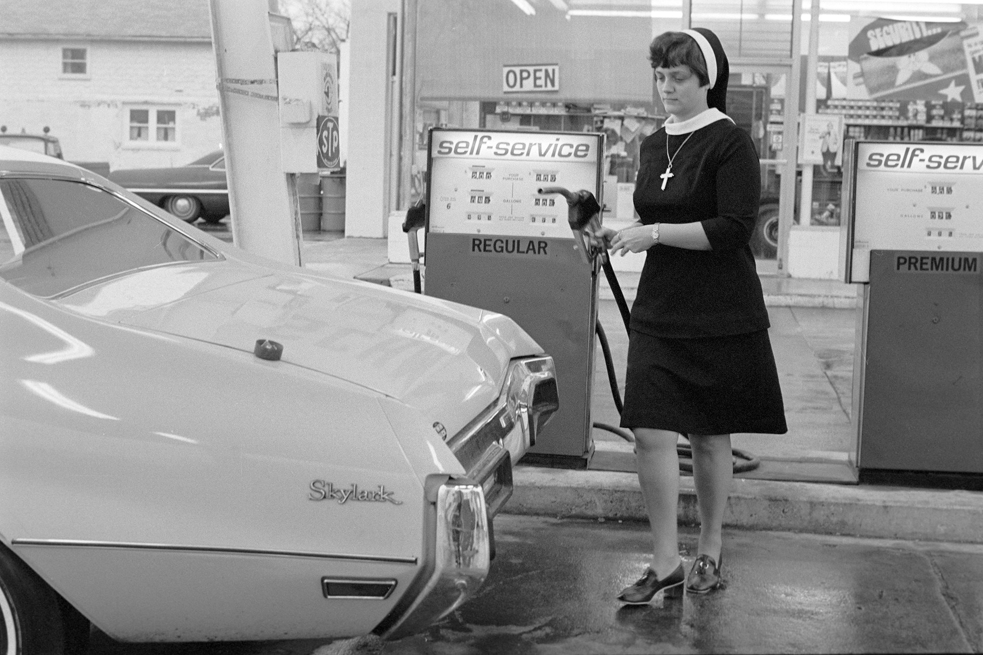 A nun wearing a habit and cross necklace carries a gas pump at a station