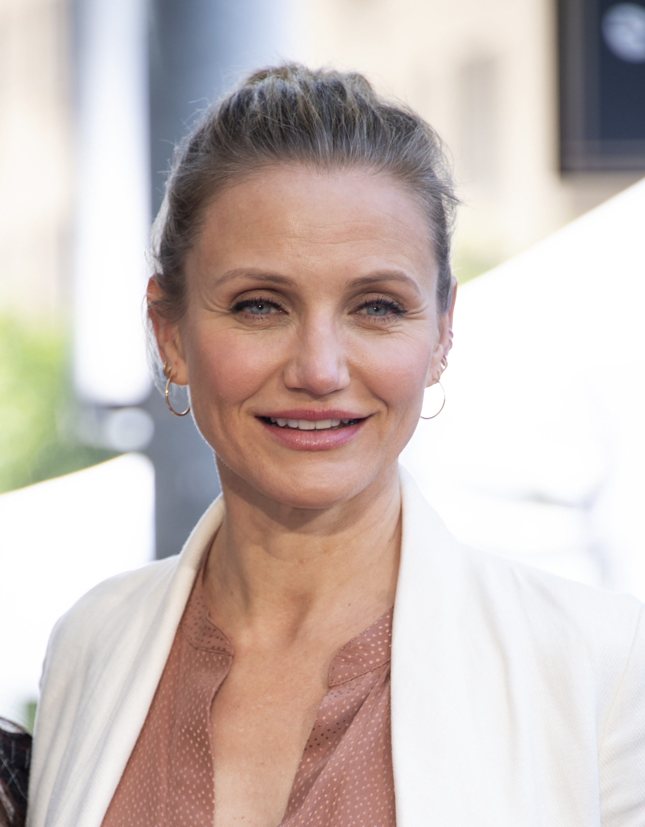 Cameron Diaz smiling in a blazer and hair loosely pulled back in a bun