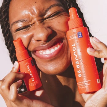 Model holding the red bottles of Tower 28 facial spray to their face