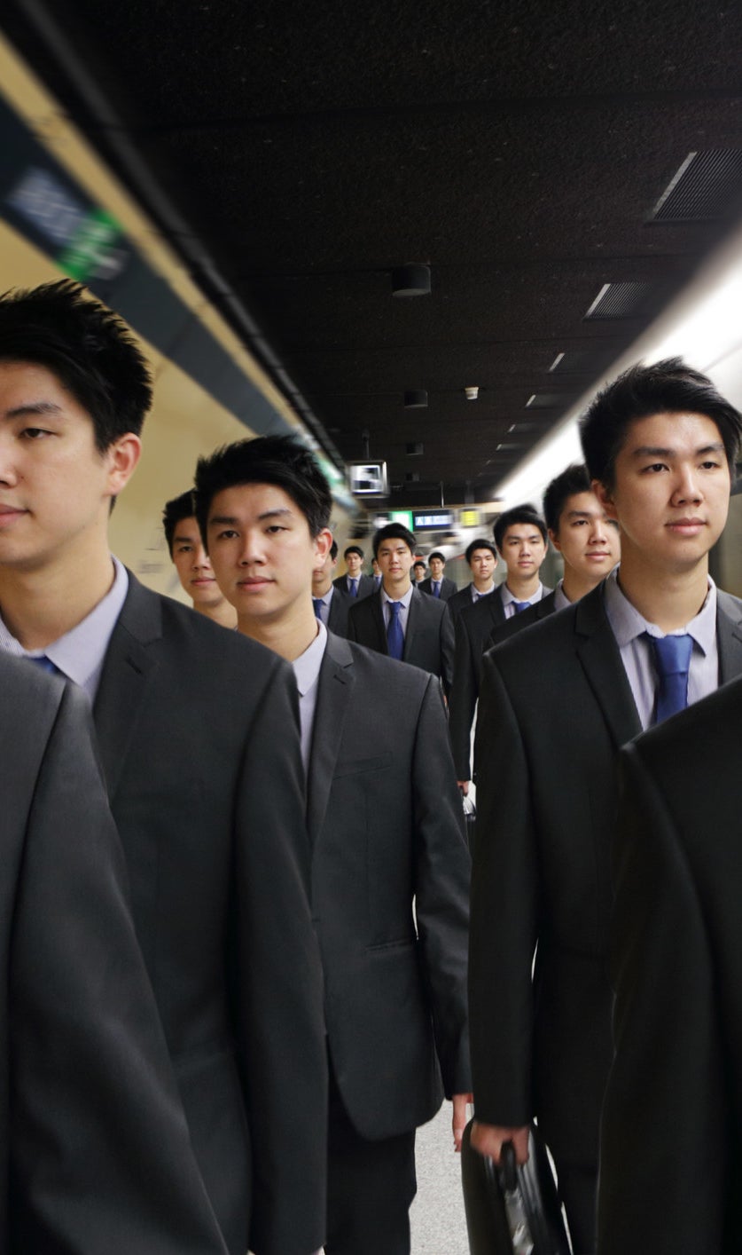 Identical men in suits walking down a subway tunnel