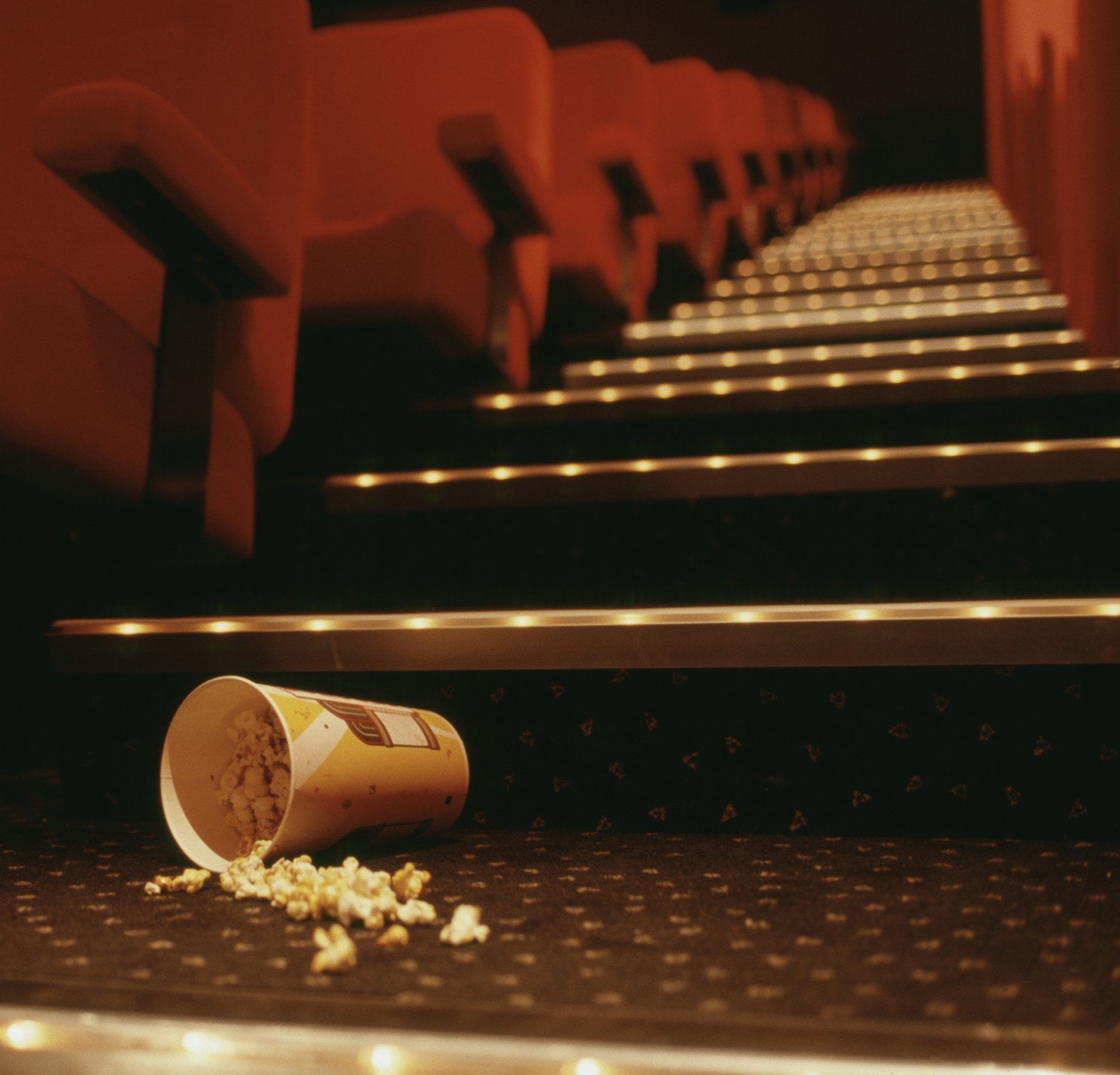 Popcorn spilling from a cup on the floor of an empty movie theater