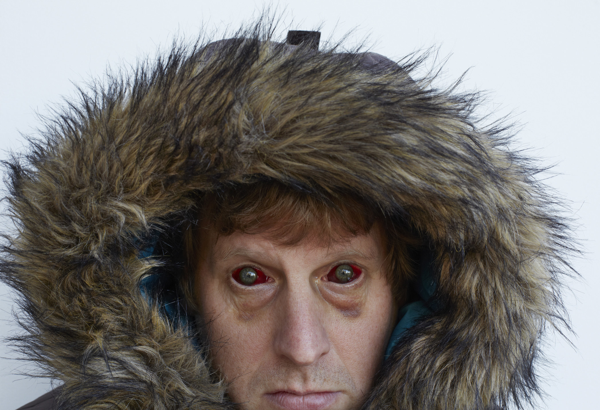 Man with red zombie-like eyes wearing a furry hood