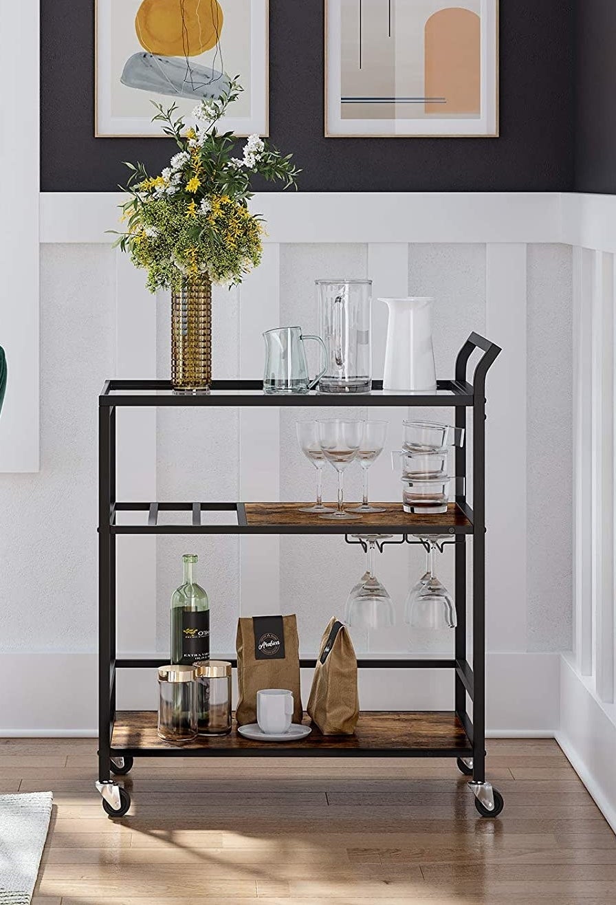 The bar cart in a dining room with bottles, coffee, wine glasses, and flowers on it
