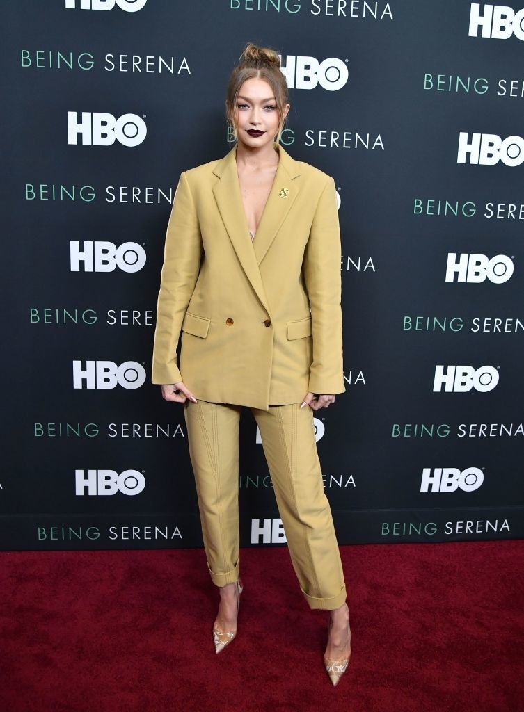Gigi wears a light-colored suit and dark lipstick with her hair in a topknot