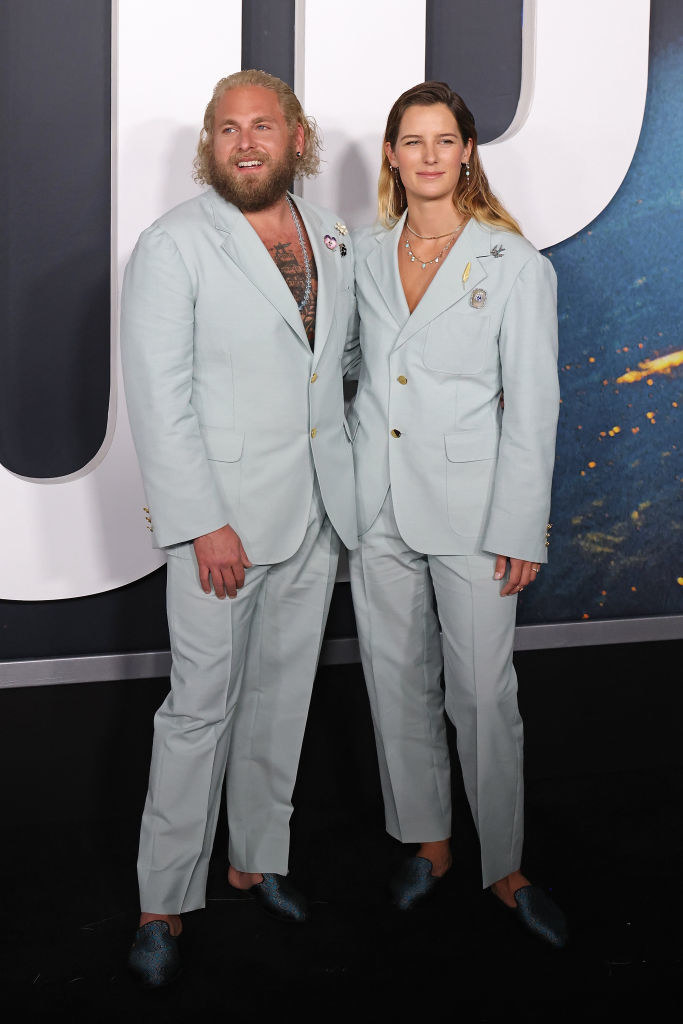 Jonah and Sarah wear matching pastel suit jackets, trousers, and shiny loafers