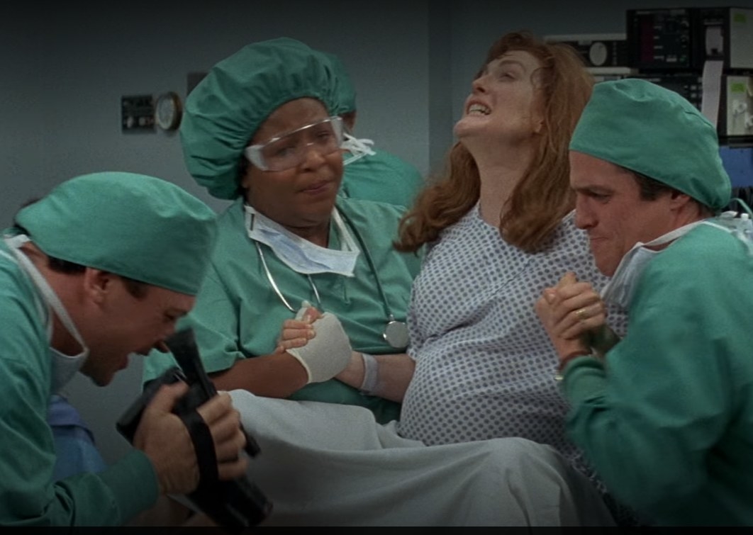 Julianne Moore as Rebecca in labor as Hugh Grant and a nurse hold her hand and Tom Arnold tries to film