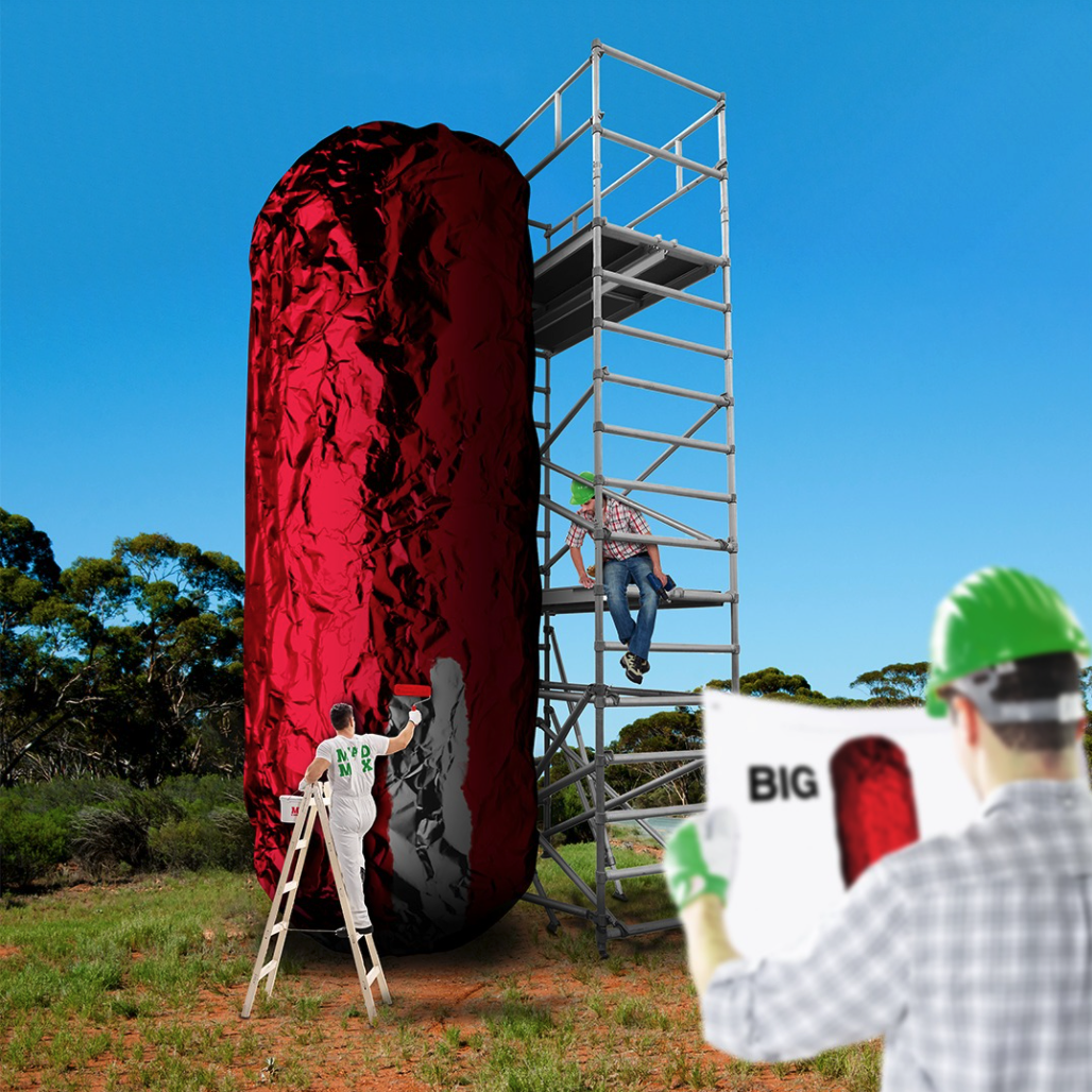 Workers painting a huge burrito upright in a field, with a man on a large platform next to it