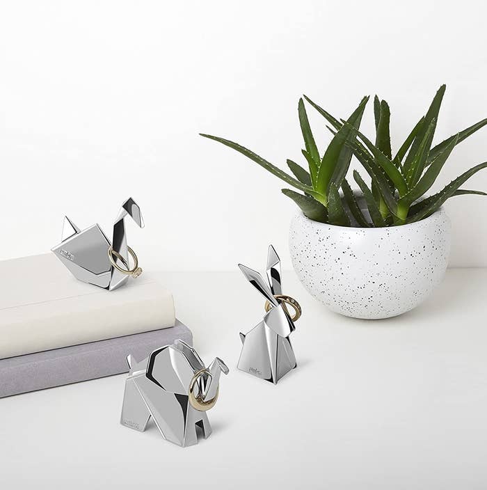 A swan, an elephant, and a bunny ring holder with rings on them next to a potted plant