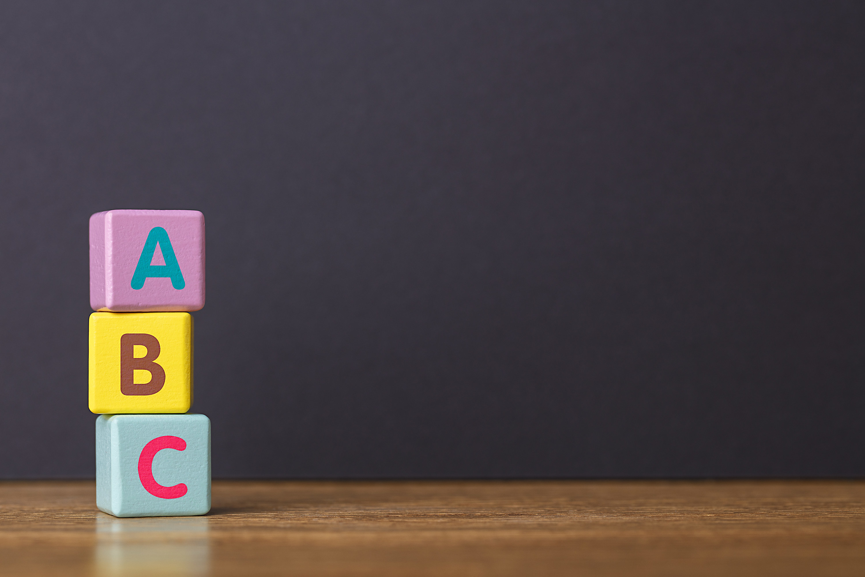 ABC letters alphabet on three toy blocks in pillar form on wooden table