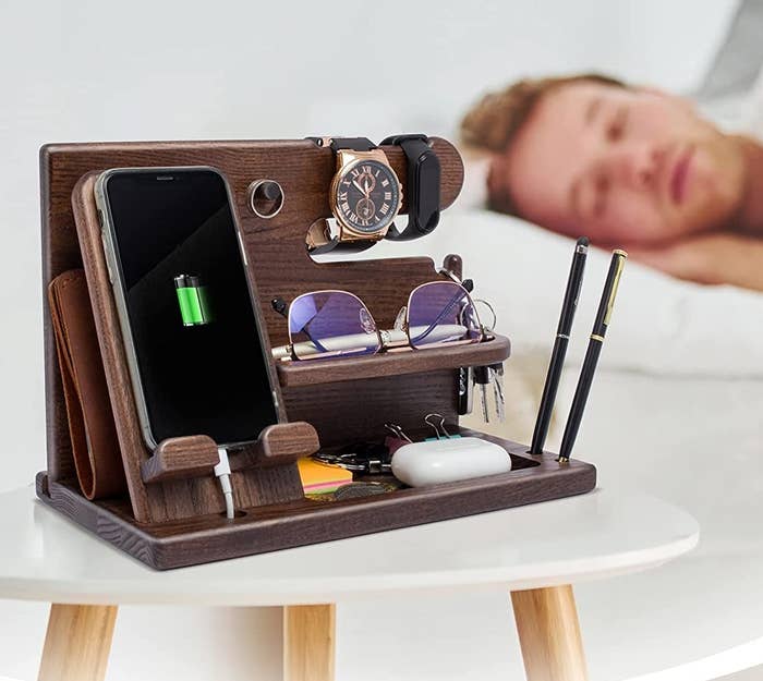 The docking station on a bedside table holding everything while a person sleeps in the background