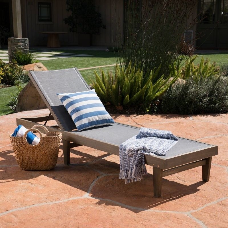 a wood chaise lounge chair with a blanket and pillow