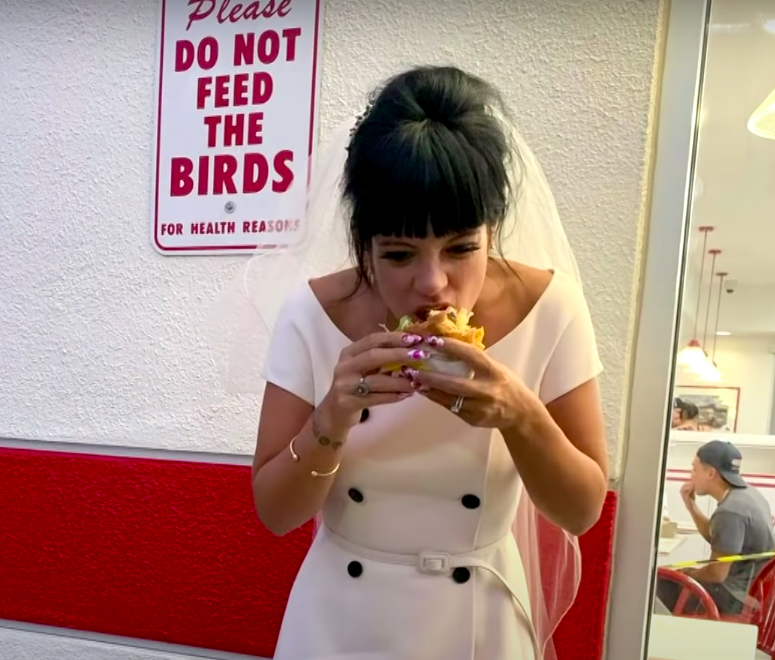 Lily in her veil and dress taking a bite of her burger